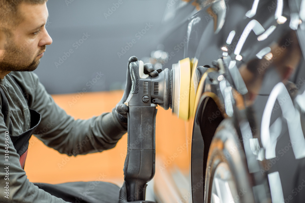 Worker polishing vehicle body with special grinder and wax from scratches at the car service station