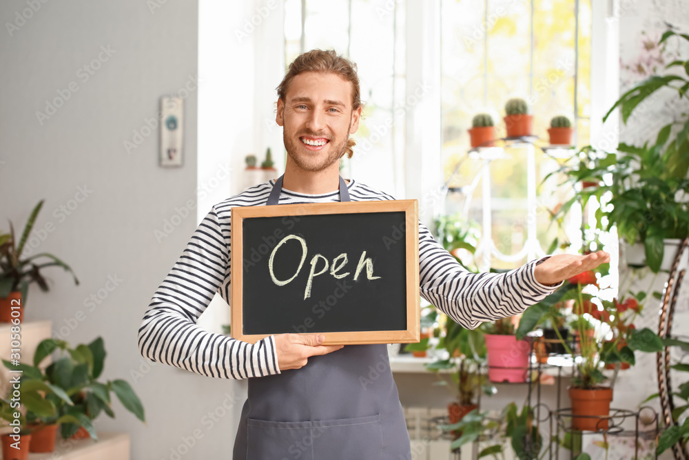 商店里拿着写有OPEN字样的黑板的男性花店老板的肖像