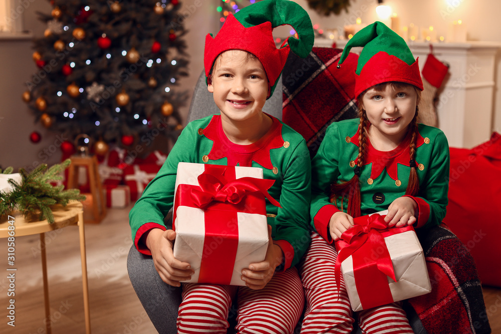 Little children in costume of elf and with gifts in room decorated for Christmas