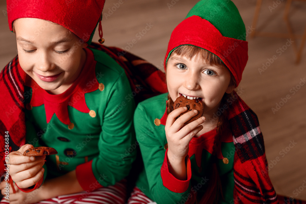 Little children in costume of elf eating cookies at home