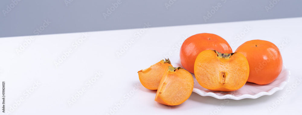 Fresh beautiful sliced sweet persimmon kaki isolated on white kitchen table with gray blue backgroun