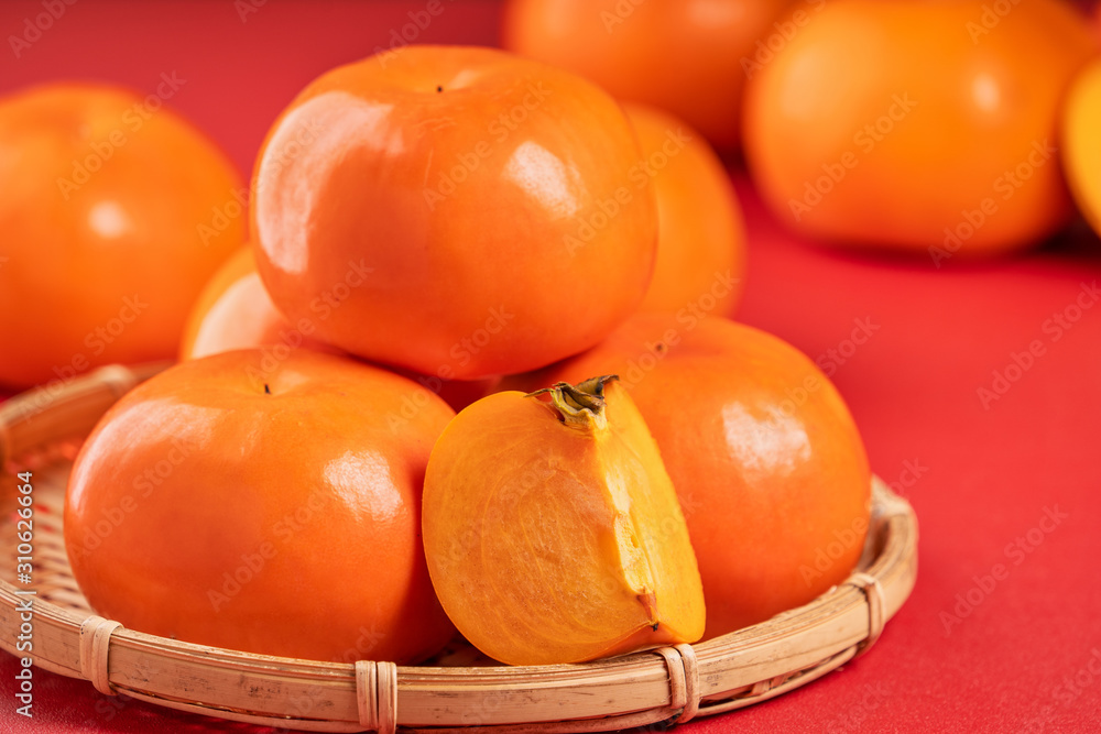 Fresh beautiful sliced sweet persimmon kaki isolated on red table background and bamboo sieve, Chine