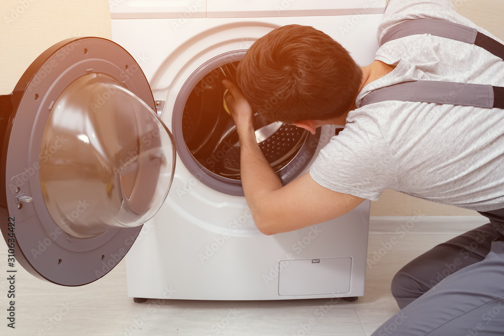 young serviceman in grey uniform repairs broken washing machine closeup