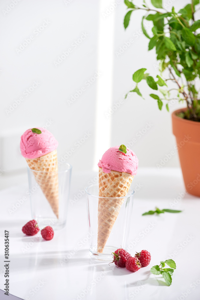 Waffle cone filled with fresh raspberry ice cream in glass cup with fresh raspberry sitting on table