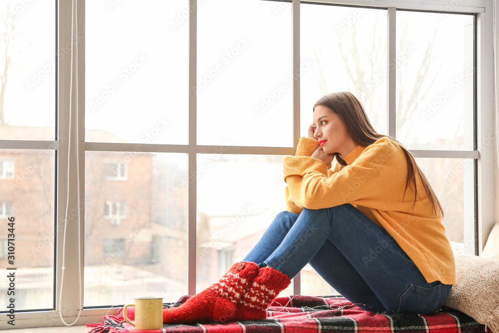 穿着冬装的年轻女子坐在家里的窗台上