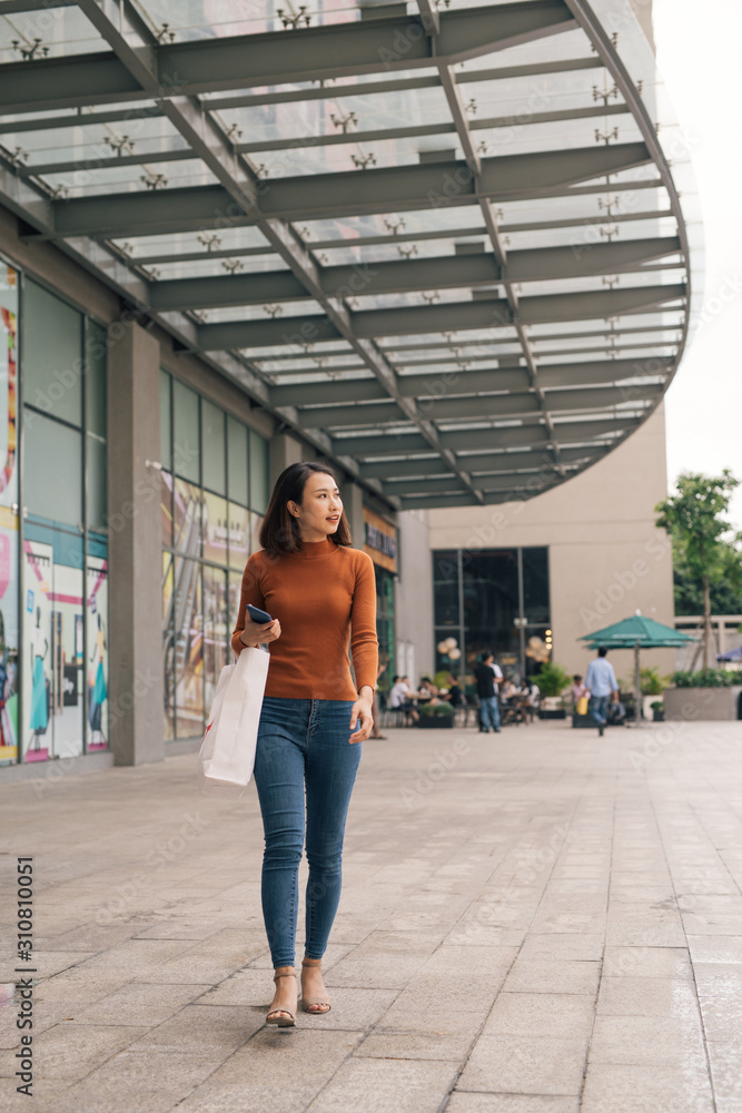 年轻快乐的亚洲女人拿着购物袋走在街上。