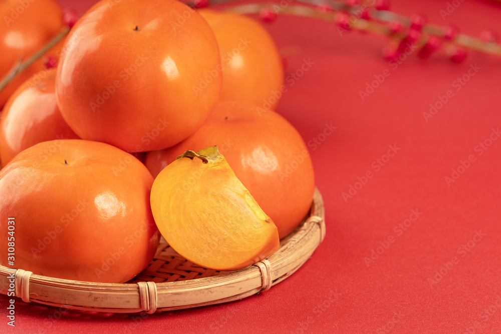 Fresh beautiful sliced sweet persimmon kaki isolated on red table background and bamboo sieve, Chine