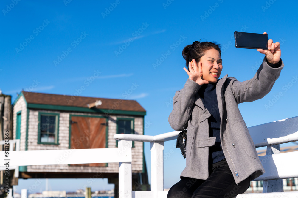 亚洲女性手持智能手机自拍旅行者，以房屋建筑为背景，亚洲照片