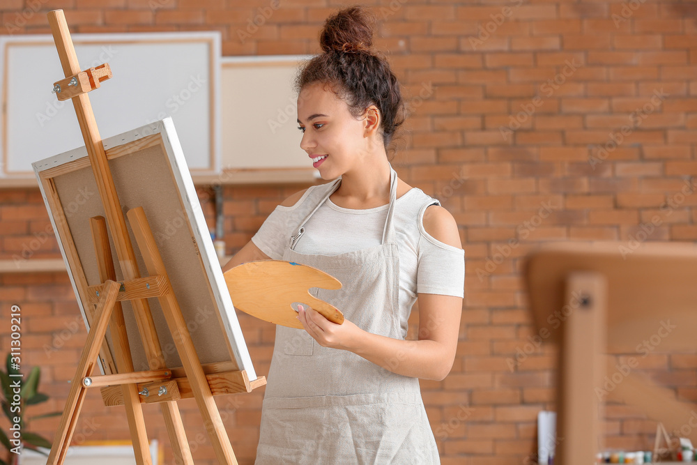 Beautiful female African-American artist painting in studio