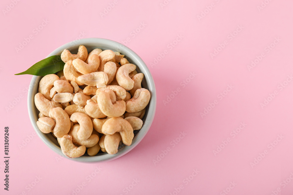 Bowl with tasty cashew nuts on color background