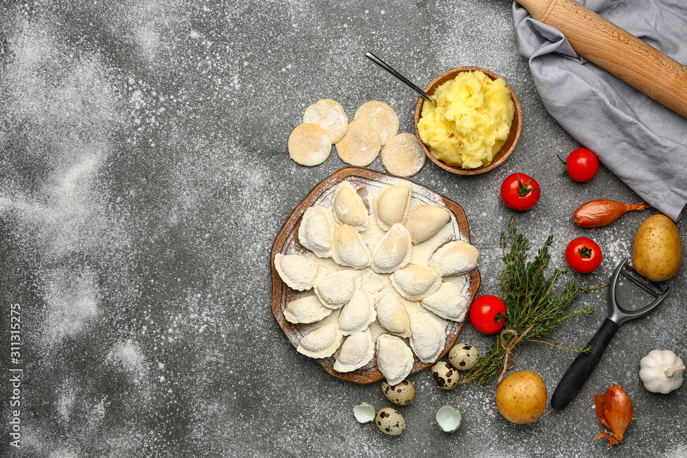 Board with raw dumplings and ingredients on grey background