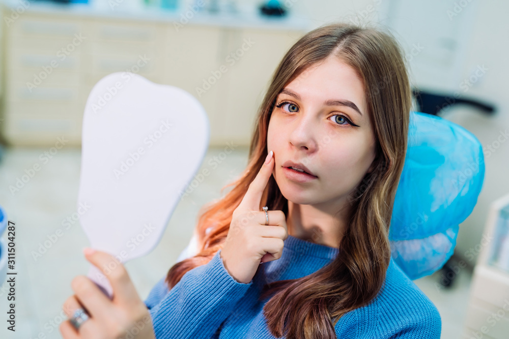 View from side of happy female patient holding a mirror and looking at camera in dental office. Youn