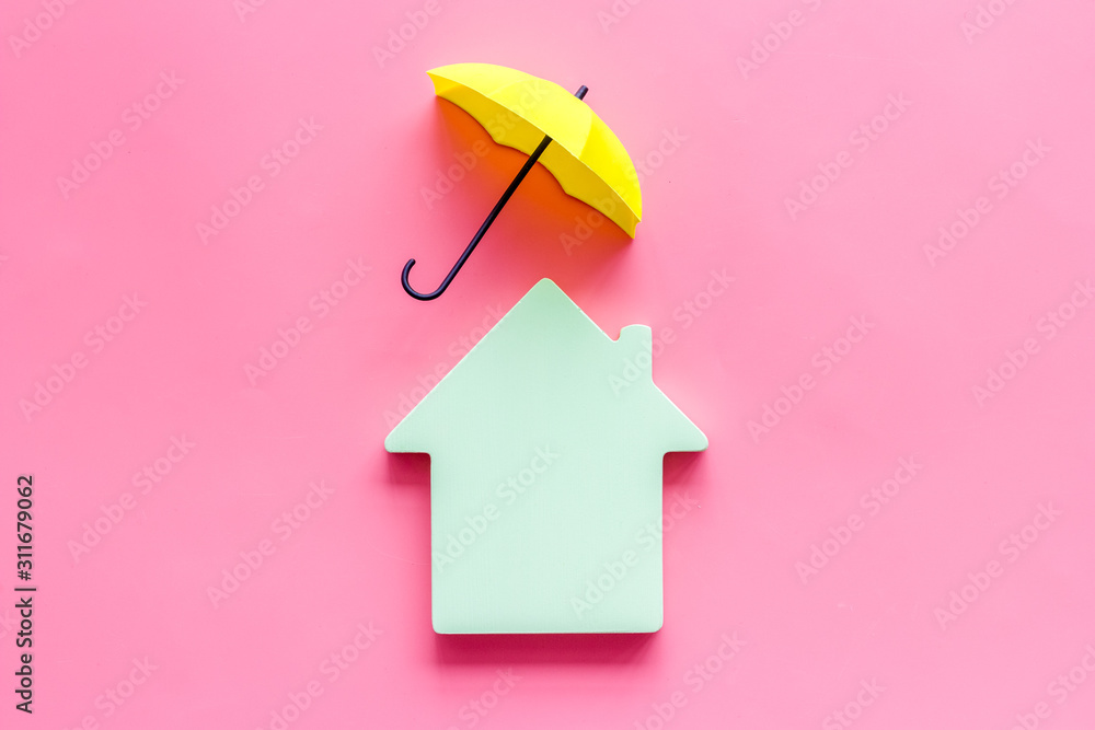 Property insurance concept. House cutout under umbrella on pink backgound top view copy space