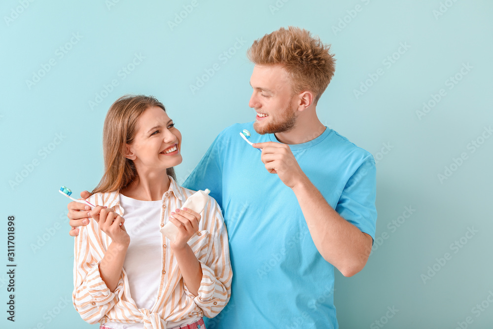 Young couple brushing teeth on color background