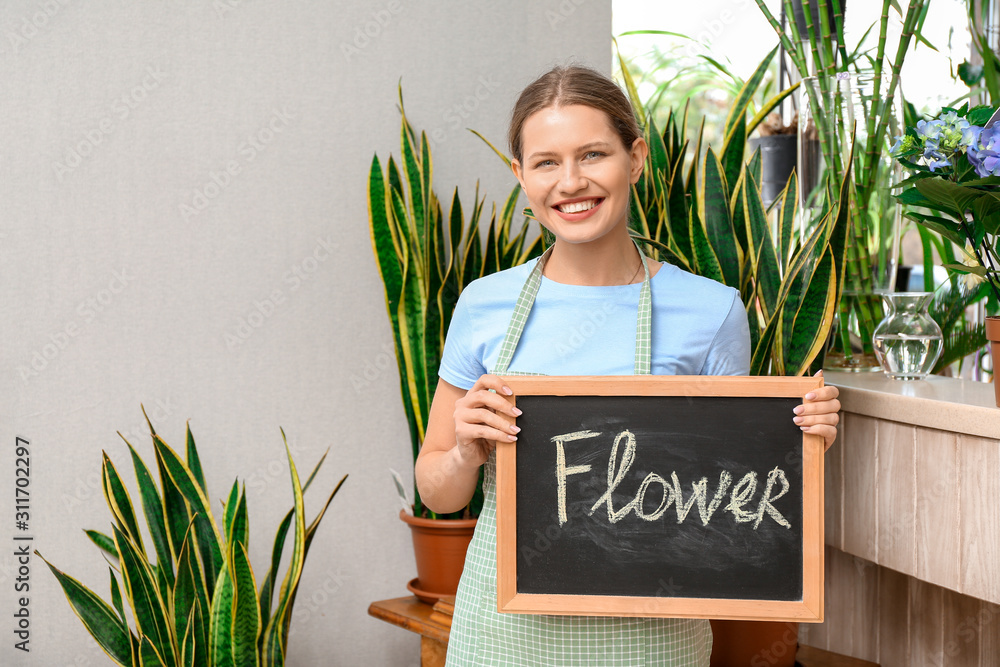 Portrait of female florist holding chalkboard with word FLOWER in shop