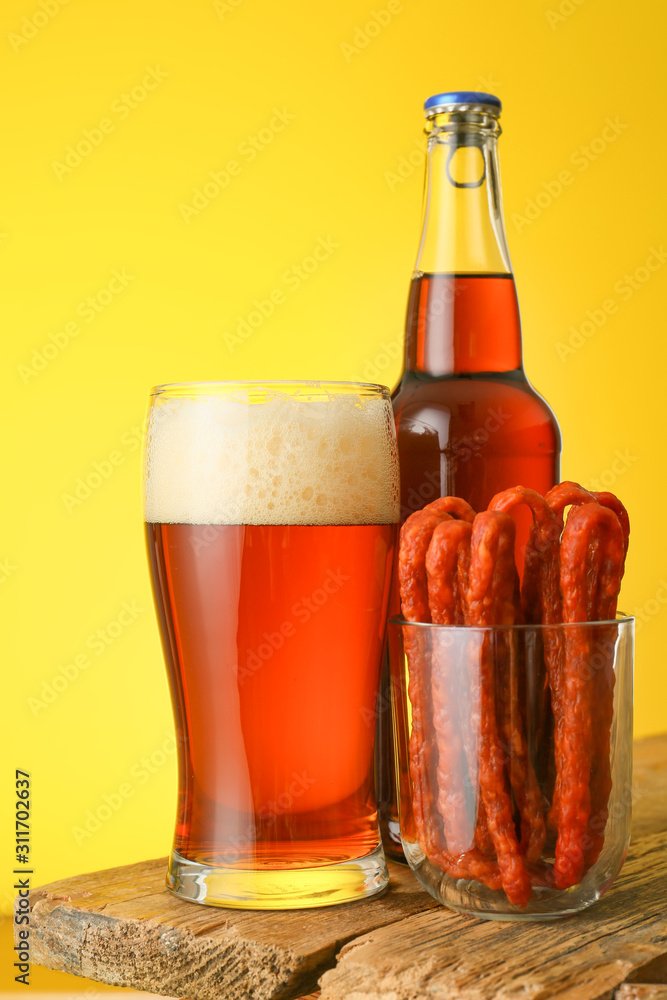 Fresh beer and sausages on table against color background