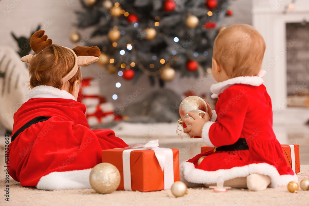 Cute little babies in Santa Claus costume and with Christmas gifts at home