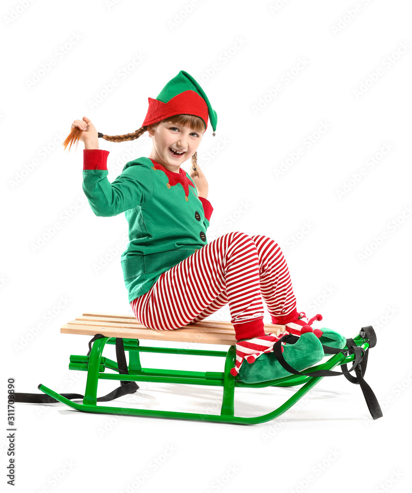 Little girl in costume of elf sitting on sledge against white background