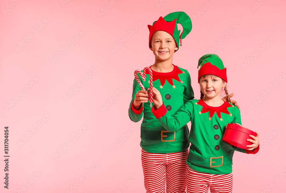 Little children in costume of elf, with gift and candy canes on color background