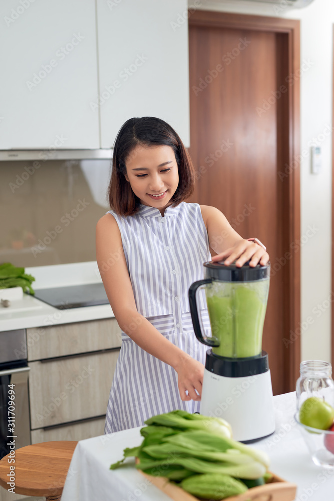 漂亮的年轻亚洲女人在厨房的搅拌机里做奶昔