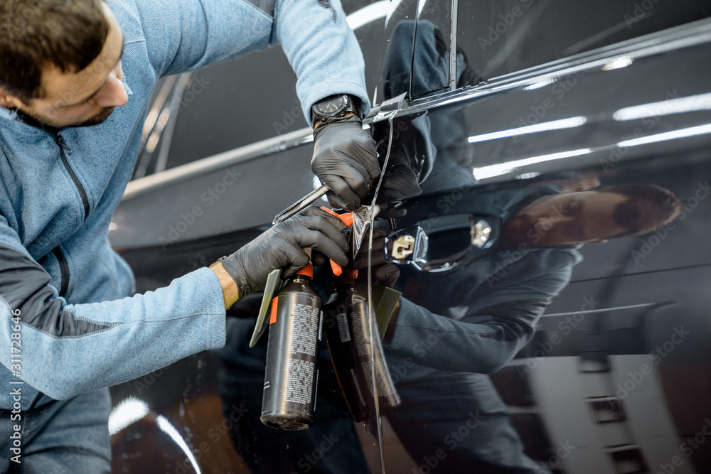 Worker trimming with cutter remains of a protective film, sticking it on a car body at the vehicle s