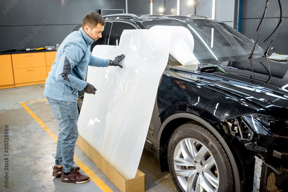 Man preparing protective film for sticking on a car body, marking it to with a pen at the vehicle se