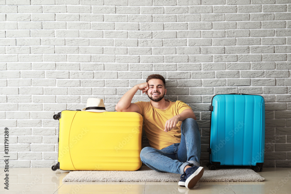 Young male tourist with luggage near brick wall