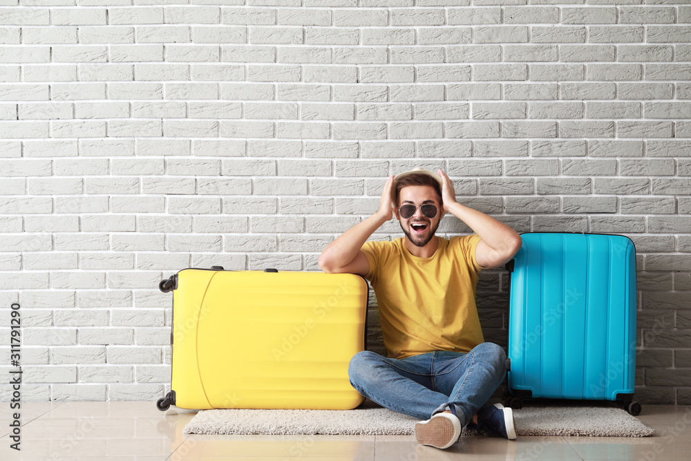 Young male tourist with luggage near brick wall