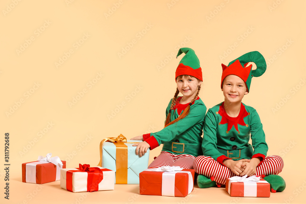 Little children in costume of elf and with gifts on color background