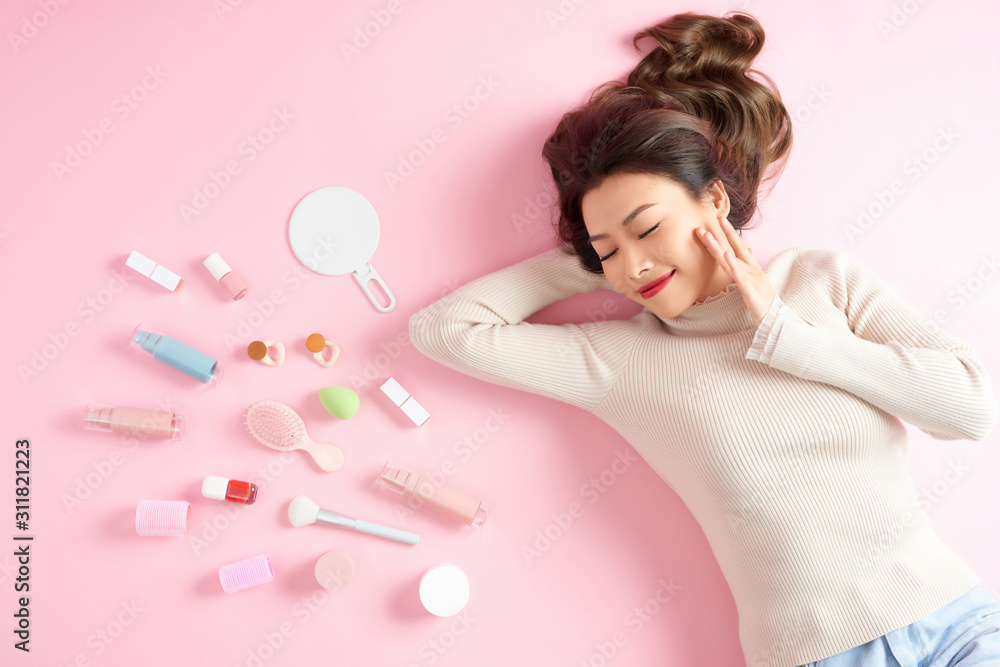 Young Asian woman sleeping on pink floor with her make up tools around. Top view