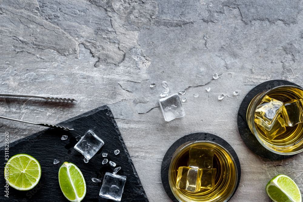 Bar background with whiskey and ice on grey stone desk top-down frame copy space