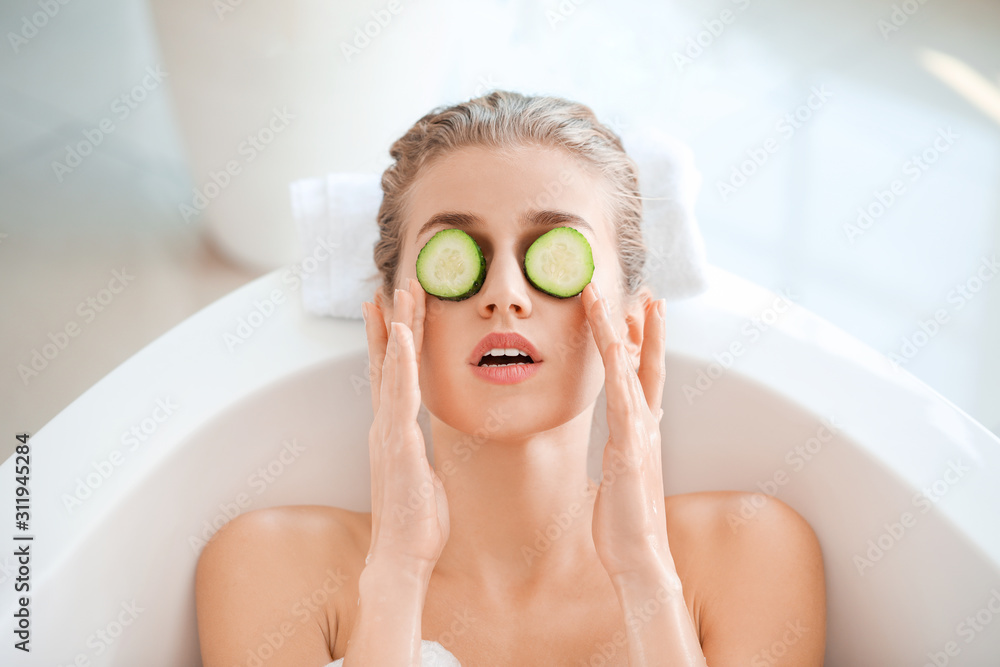 Beautiful young woman with cucumber slices lying in bathroom