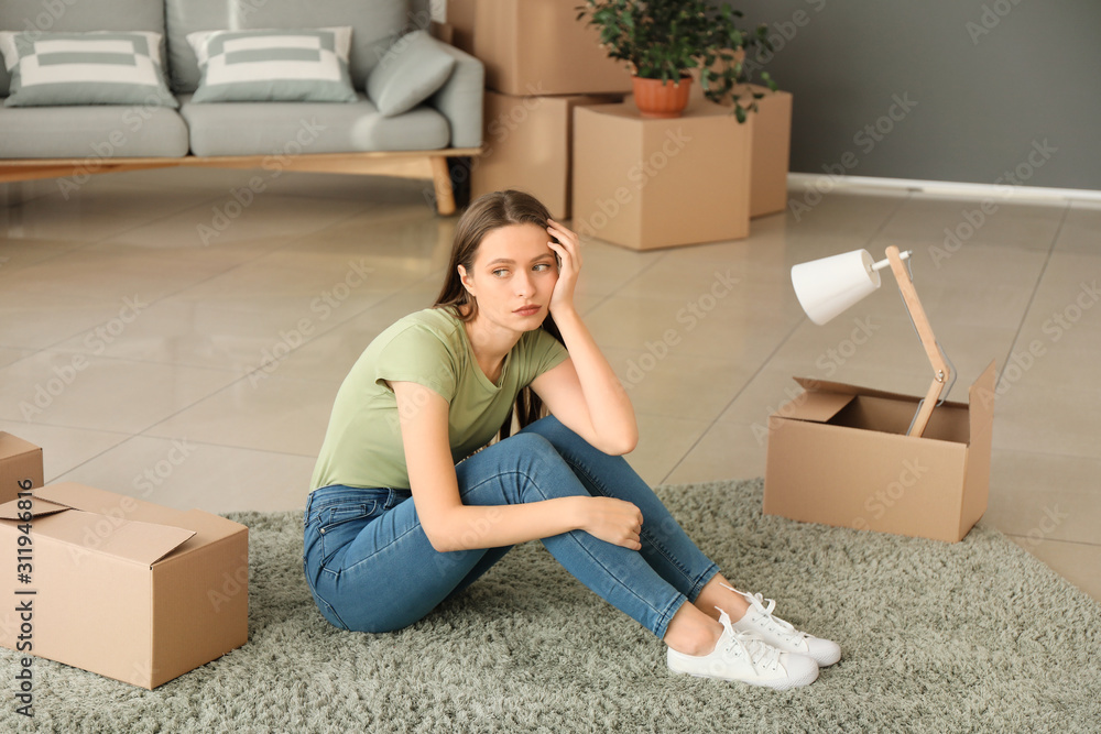 Sad young woman with belongings in new house