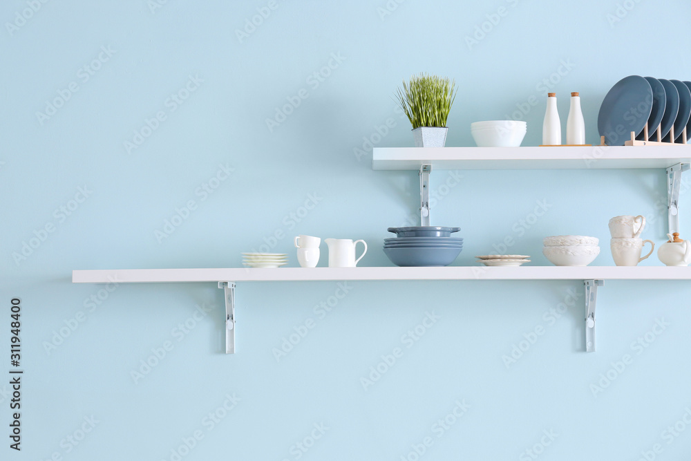 Shelves with tableware hanging on color wall