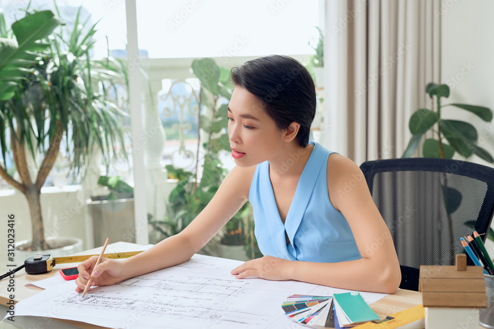 Asian female architect studying plans in office