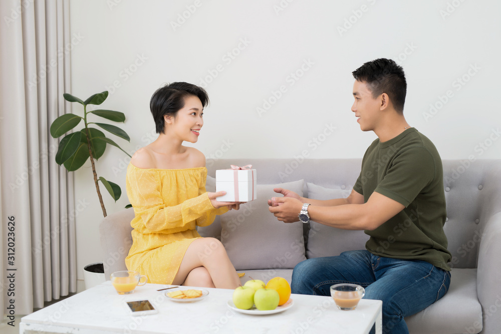 Handsome young Asian man giving present to beautiful woman at home