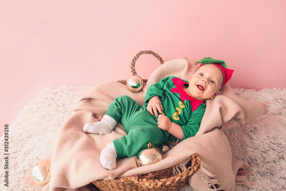 Little baby in costume of elf lying in basket near color wall