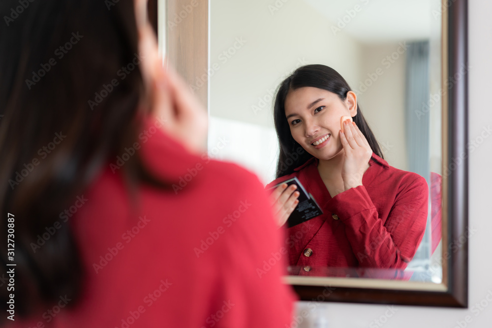 美丽的亚洲女人穿着红色衣服，把粉扑放在卧室的镜子里