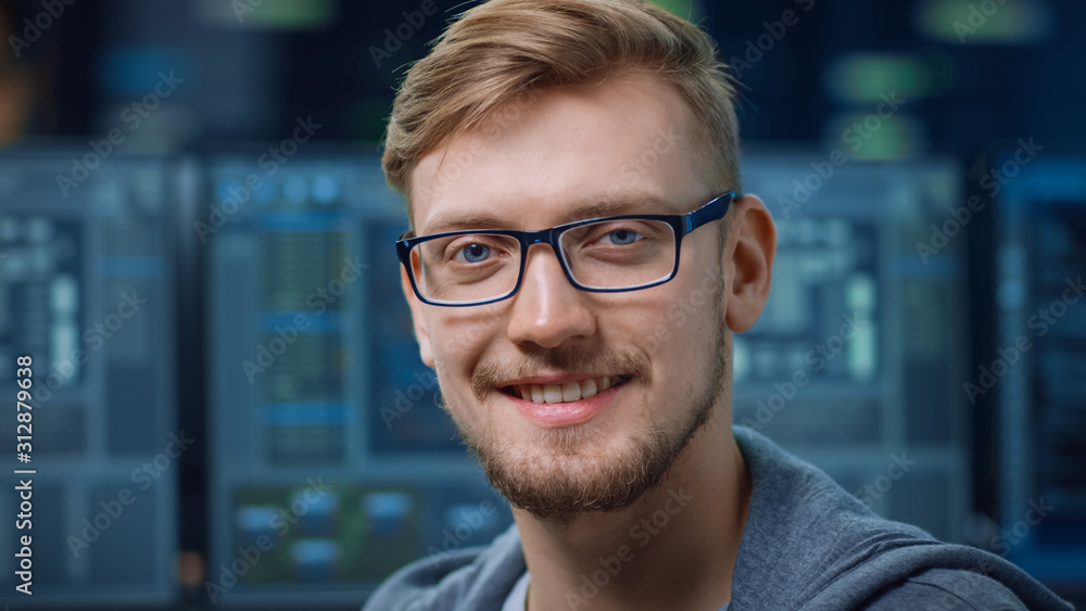 Portrait of a Smart and Handsome IT Specialist Wearing Glasses Smiles at the Camera. In the Backgrou