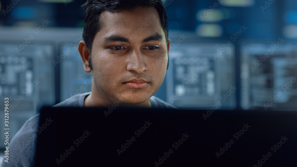 Portrait of a Smart and Handsome IT Specialist Working on a Personal Computer. In the Background Unf