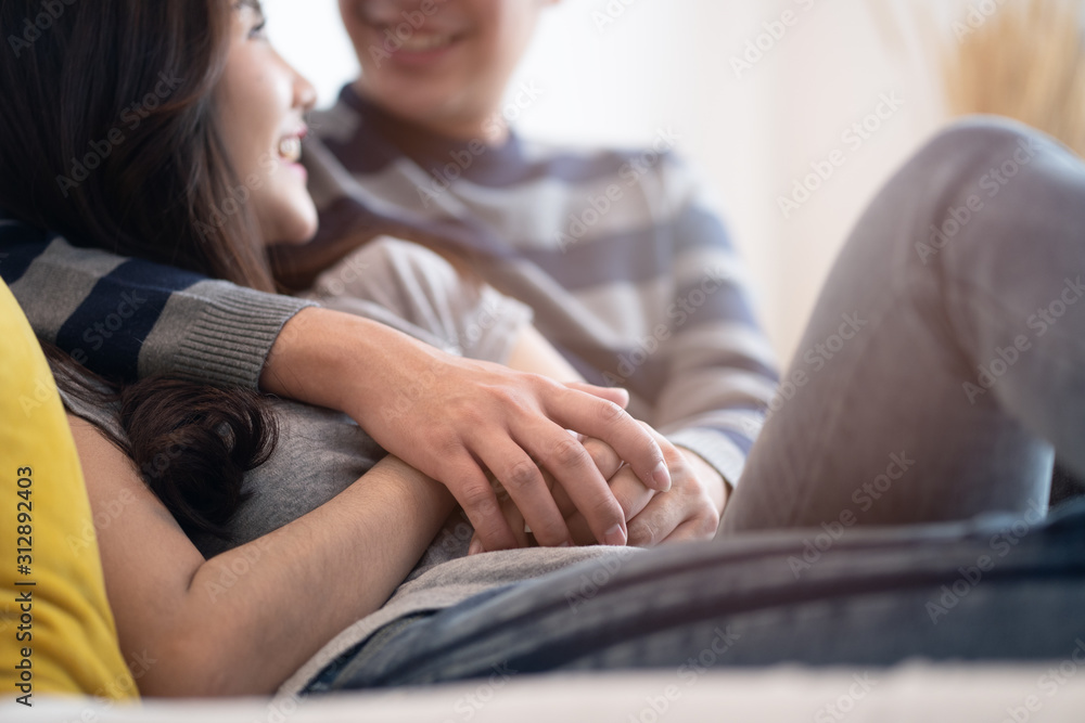 可爱的亚洲夫妇坐在卧室的床上，幸福地交谈。男孩拥抱女孩和