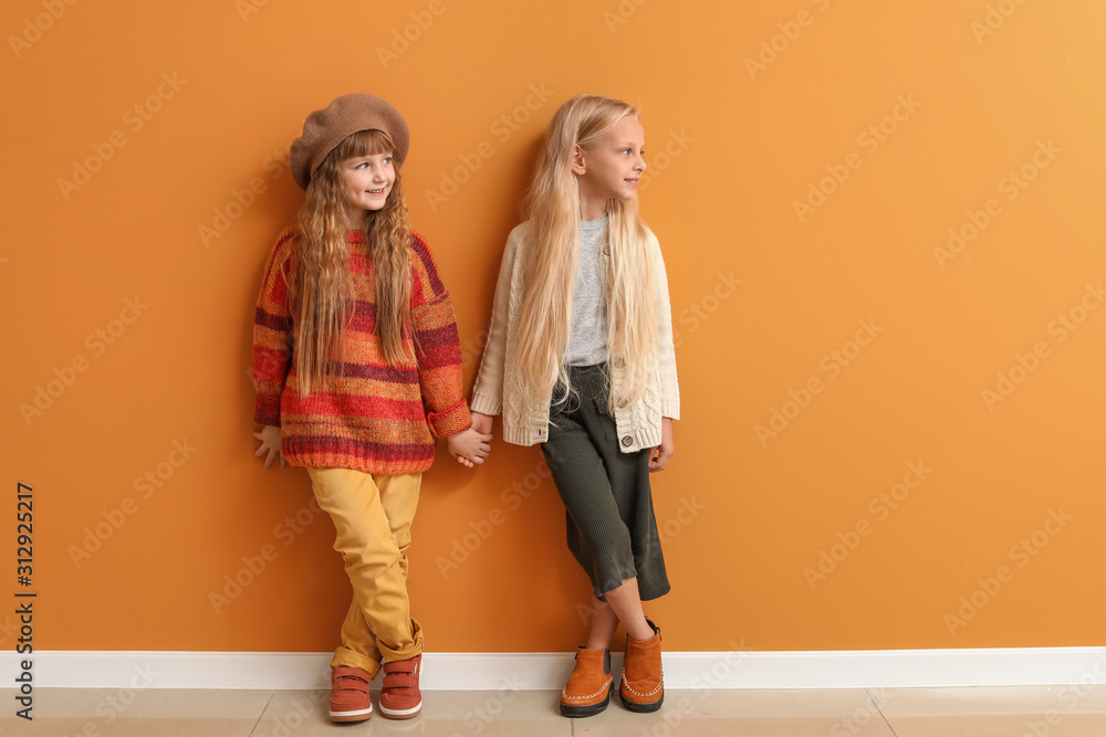 Cute little girls in autumn clothes near color wall