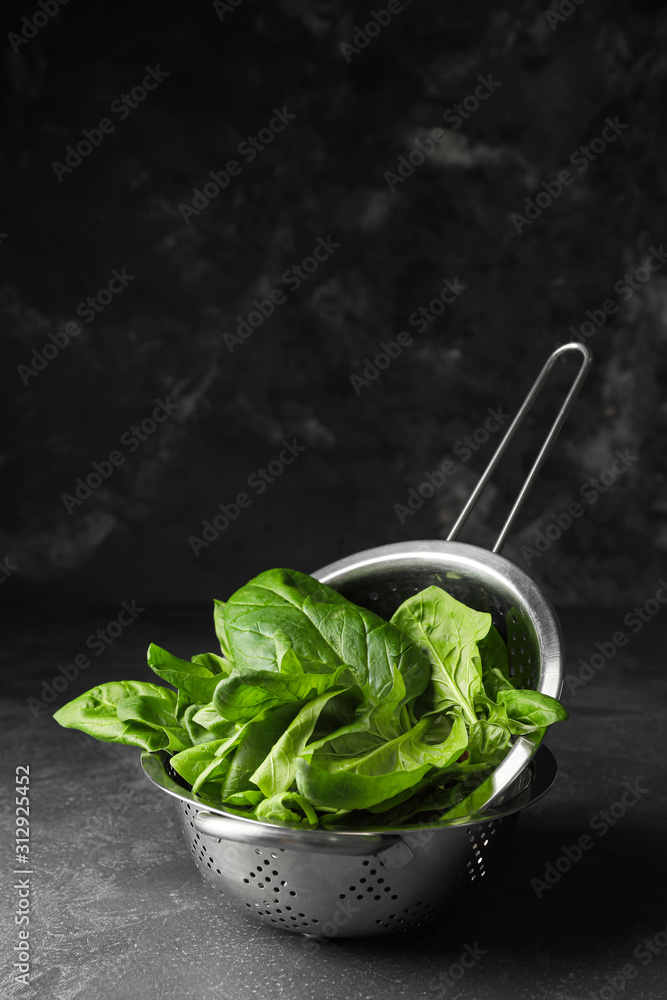 Colander with fresh spinach on table