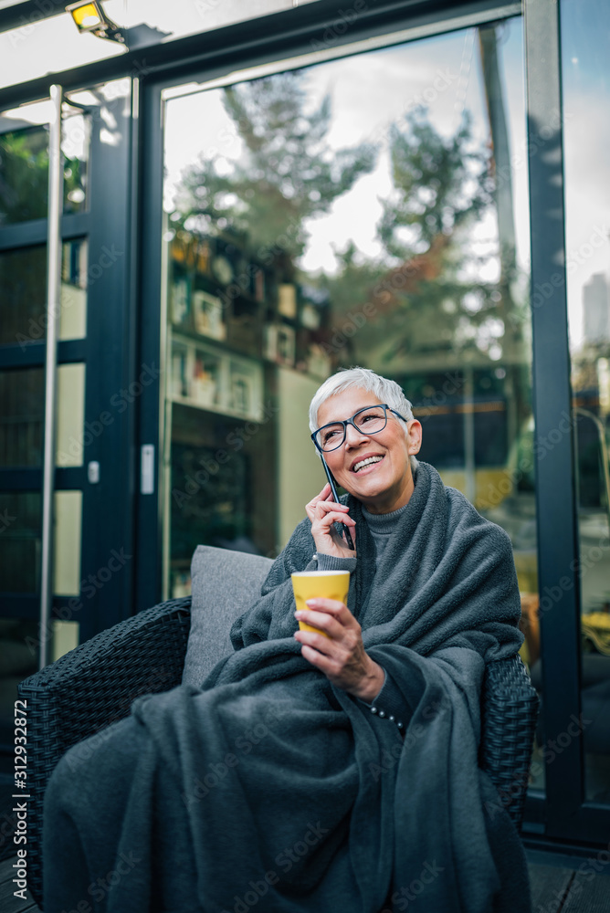 一个快乐的成熟女人的画像，她裹着毯子坐在院子里，对着漂亮的pho说话