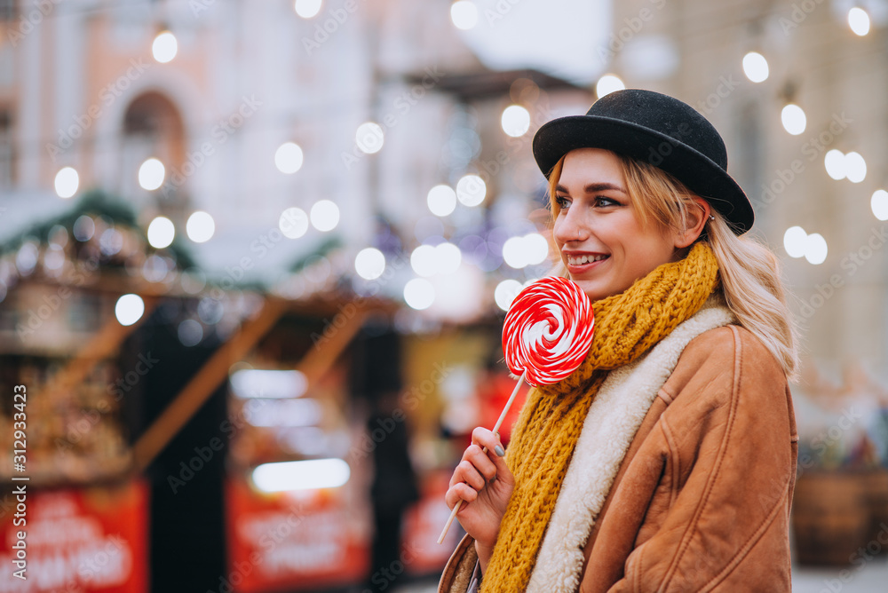 Winter portrait of a girl visiting traditional Christmas fair, holding lollipop.