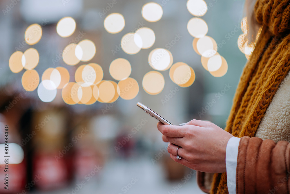 Close-up image of a woman using smart phone visiting outdoors Christmas market.