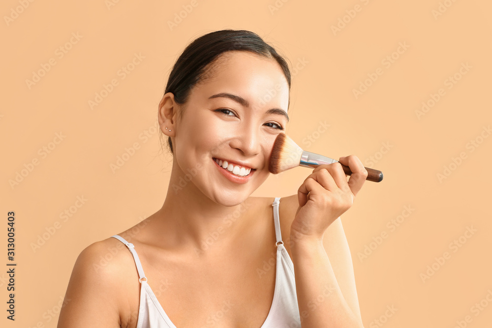 Portrait of young Asian woman with makeup brush on color background