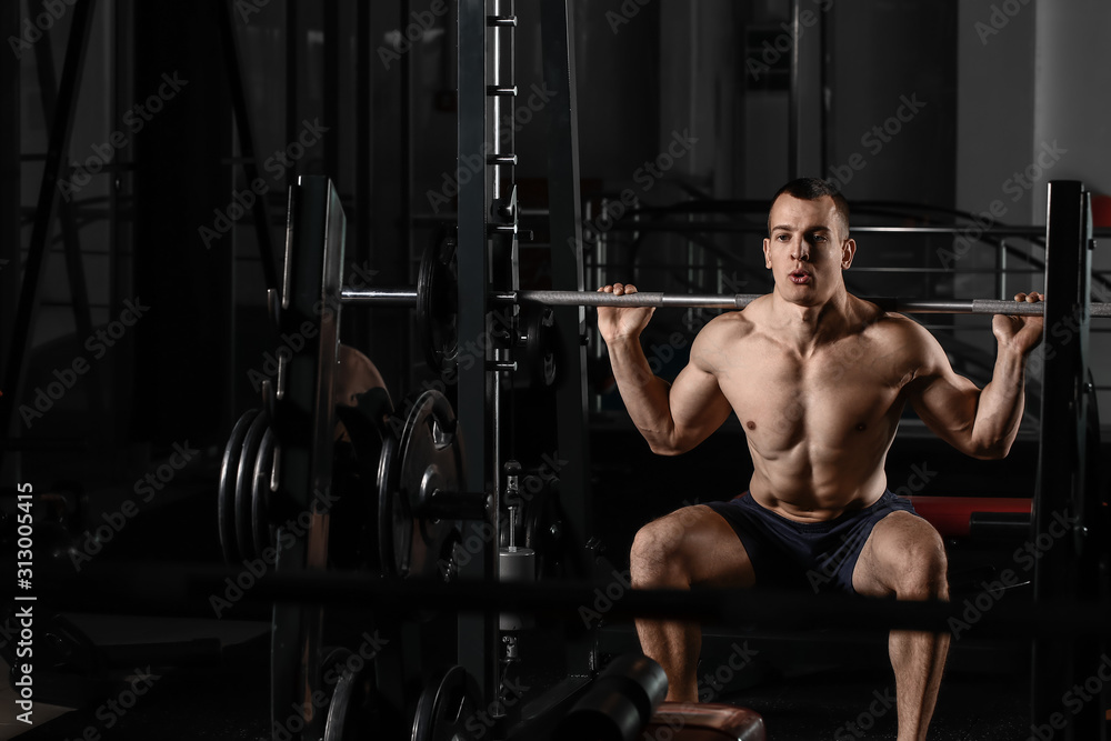 Sporty muscular man training with barbell in gym