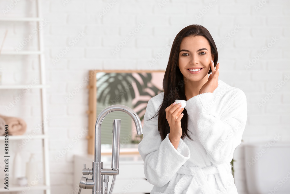 Beautiful young woman applying cream in bathroom