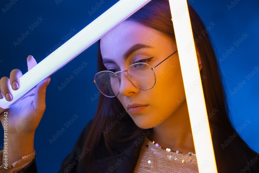 Toned portrait of beautiful woman with neon lamps on dark color background